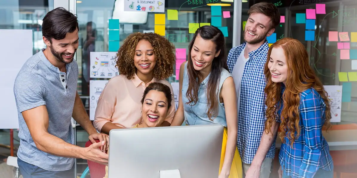Team members smiling and collaborating around a desktop computer