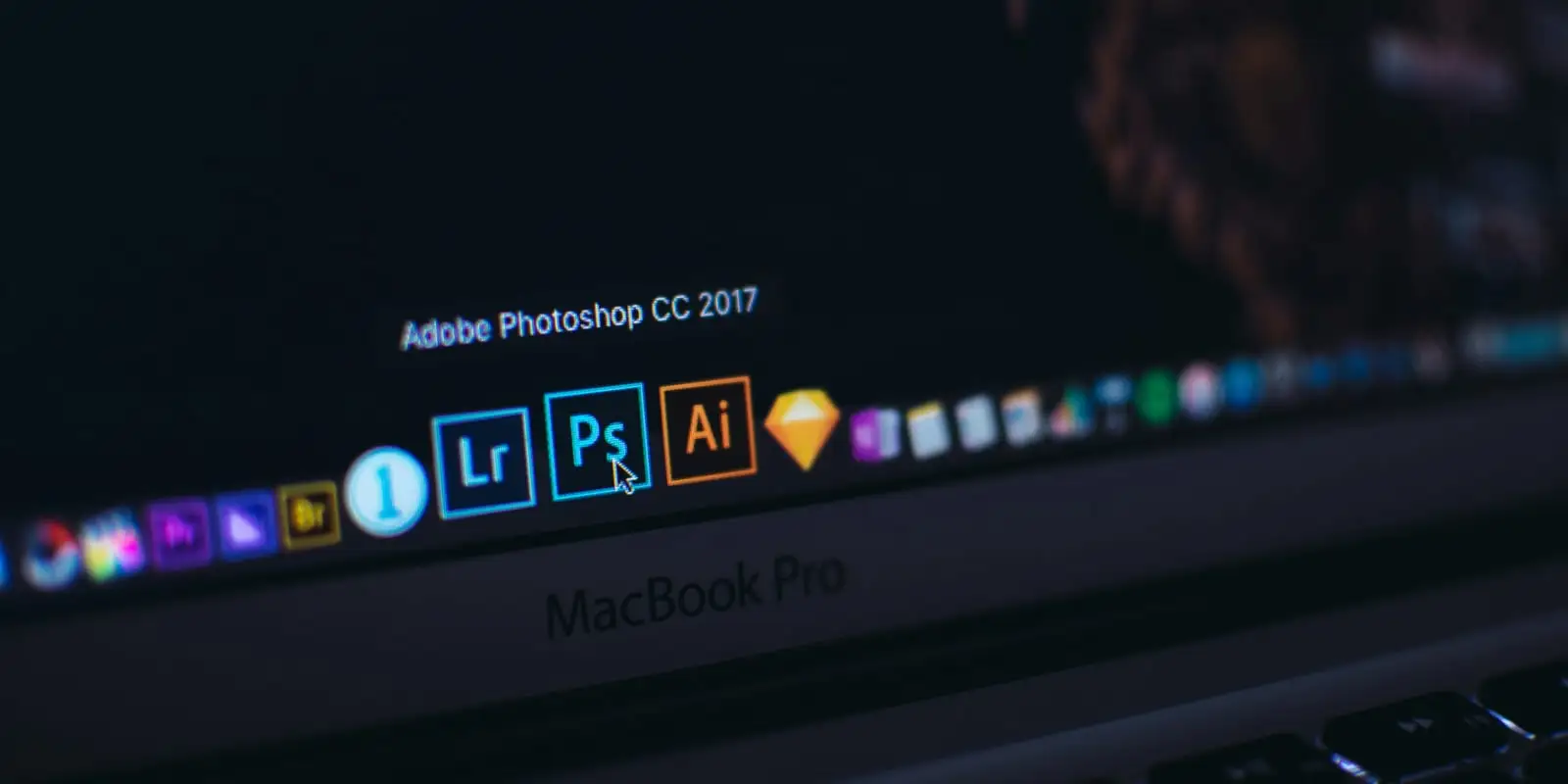 Close-up of a laptop screen showing Adobe Photoshop and other creative app icons