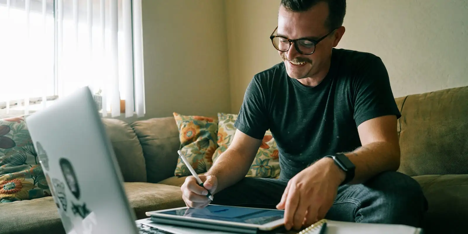 Designer sketching on a tablet while working from a laptop at home